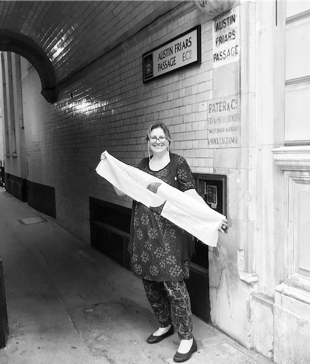 Author holding stitched fabric under a sign that reads Austin Friars Passage
