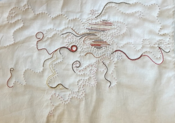 White fabric, quilted with brown, cream, orange, red, grey and black thread in a random curving design