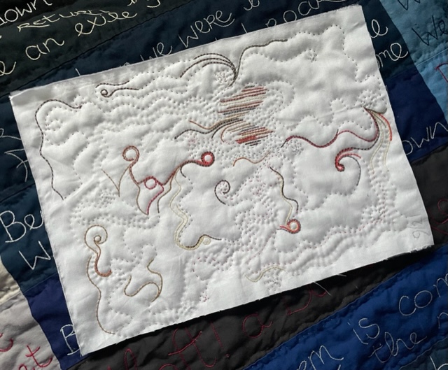 A white piece of fabric, quilted and embroidered in a curving pattern, in shades of brown, orange, grey, cream, and red